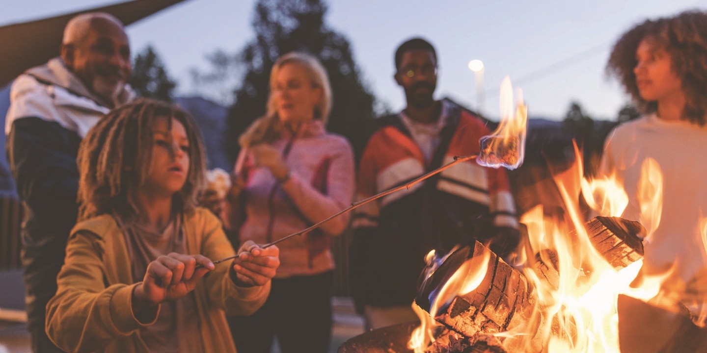 Child roasting marshmallow at a campfire, surrounded by a communal gathering